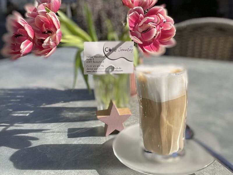 Latte Macciato Glas vor Vase mit Tulpen mit Visitenkarte Café Sonntag +