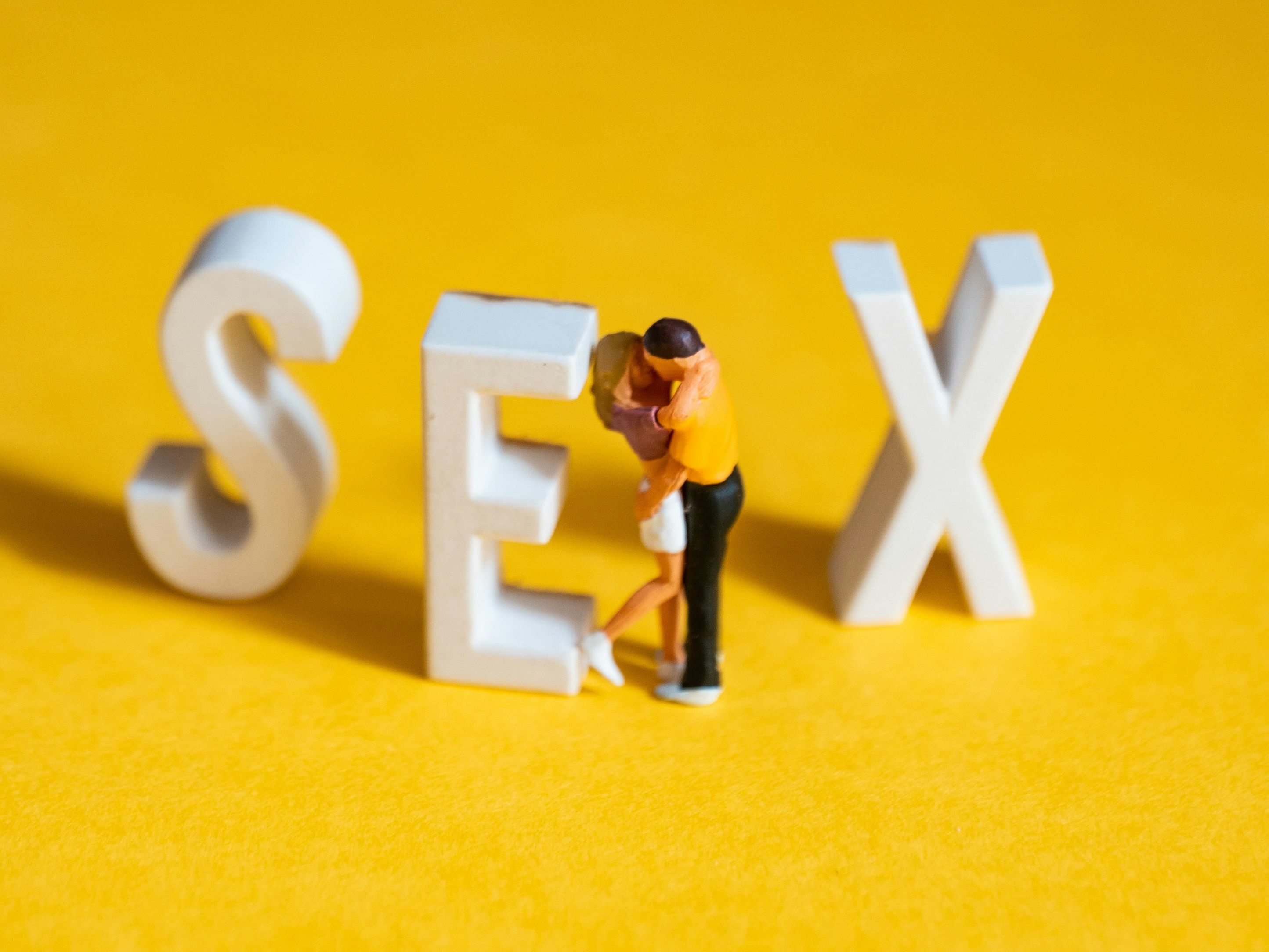 Vor den Buchstaben Sex steht ein Miniatur Päärchen und küsst sich