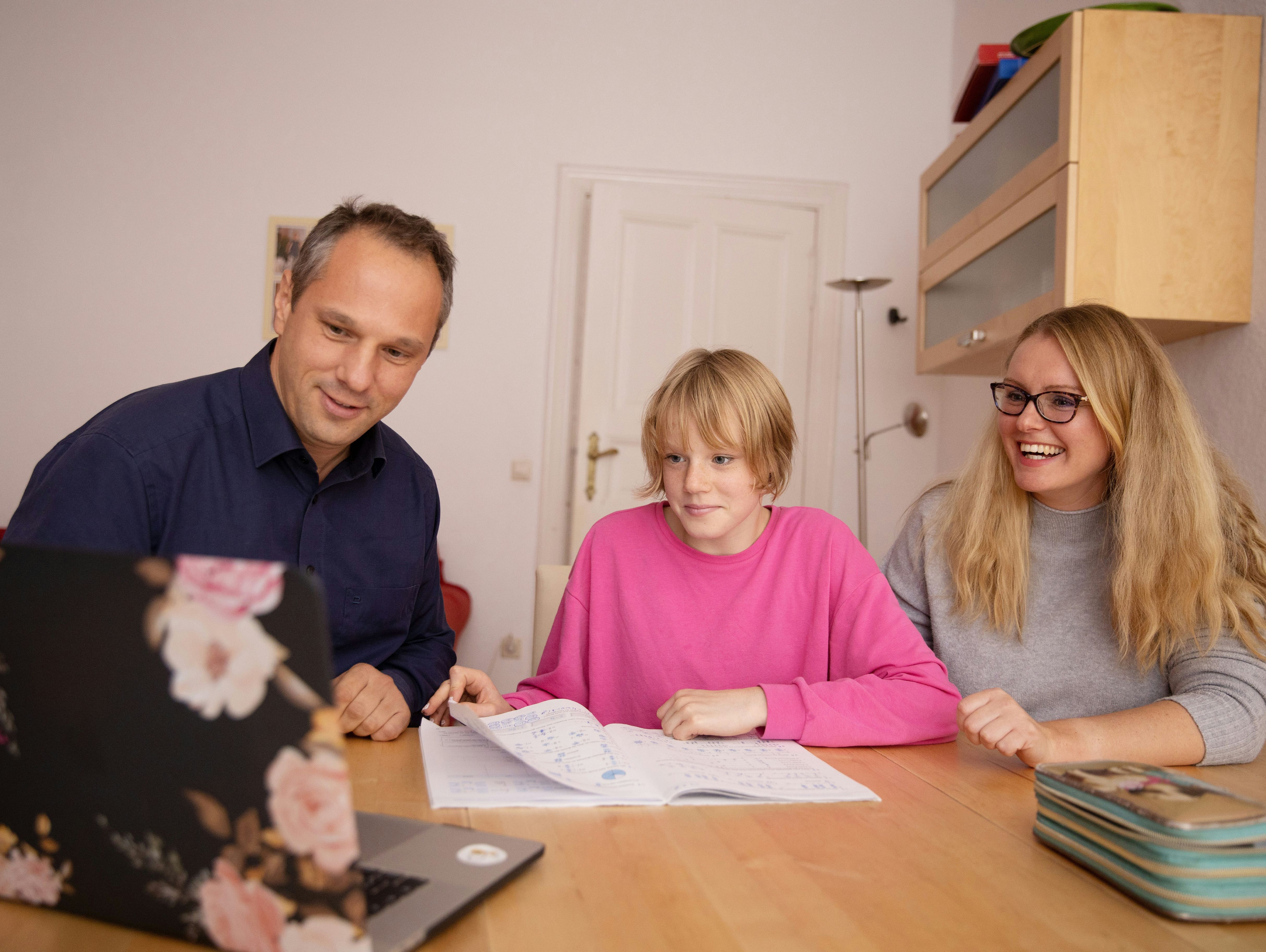 Vater und Mutter sitzen mit Kind am Tisch und machen gemeinsam Hausaufgaben