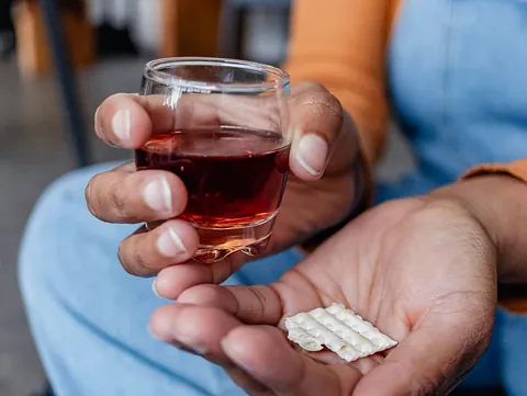 2 Hände mit Alkohol im Glas und Tabletten