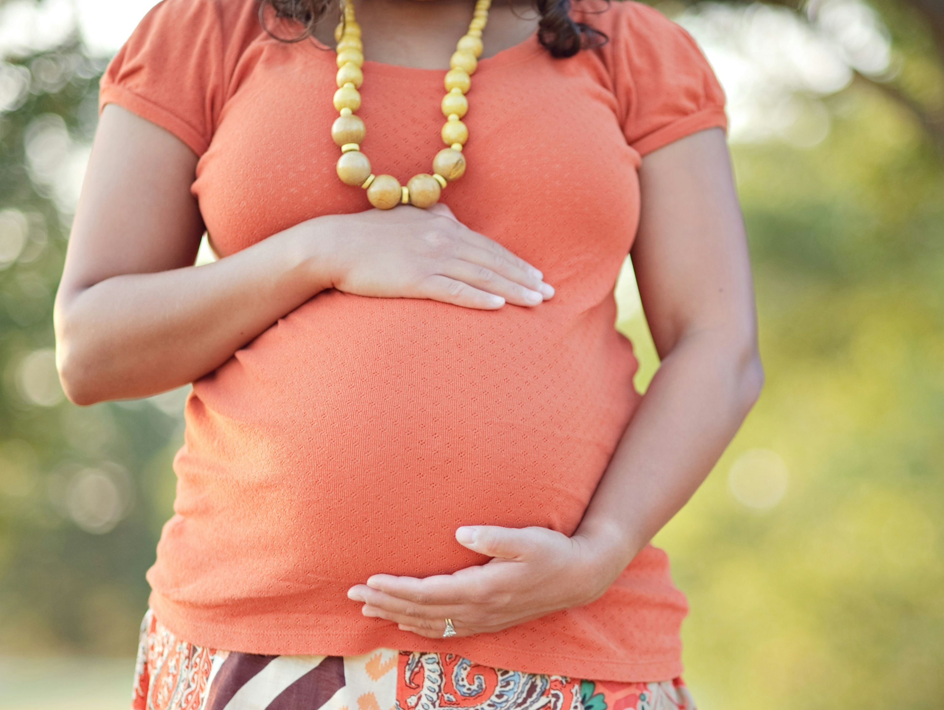 Schwangere rahmt ihren Bauch mit den Händen ein