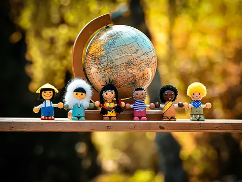 Kleine Püppchen unterschiedlicher Nationalität stehen vor einem Globus